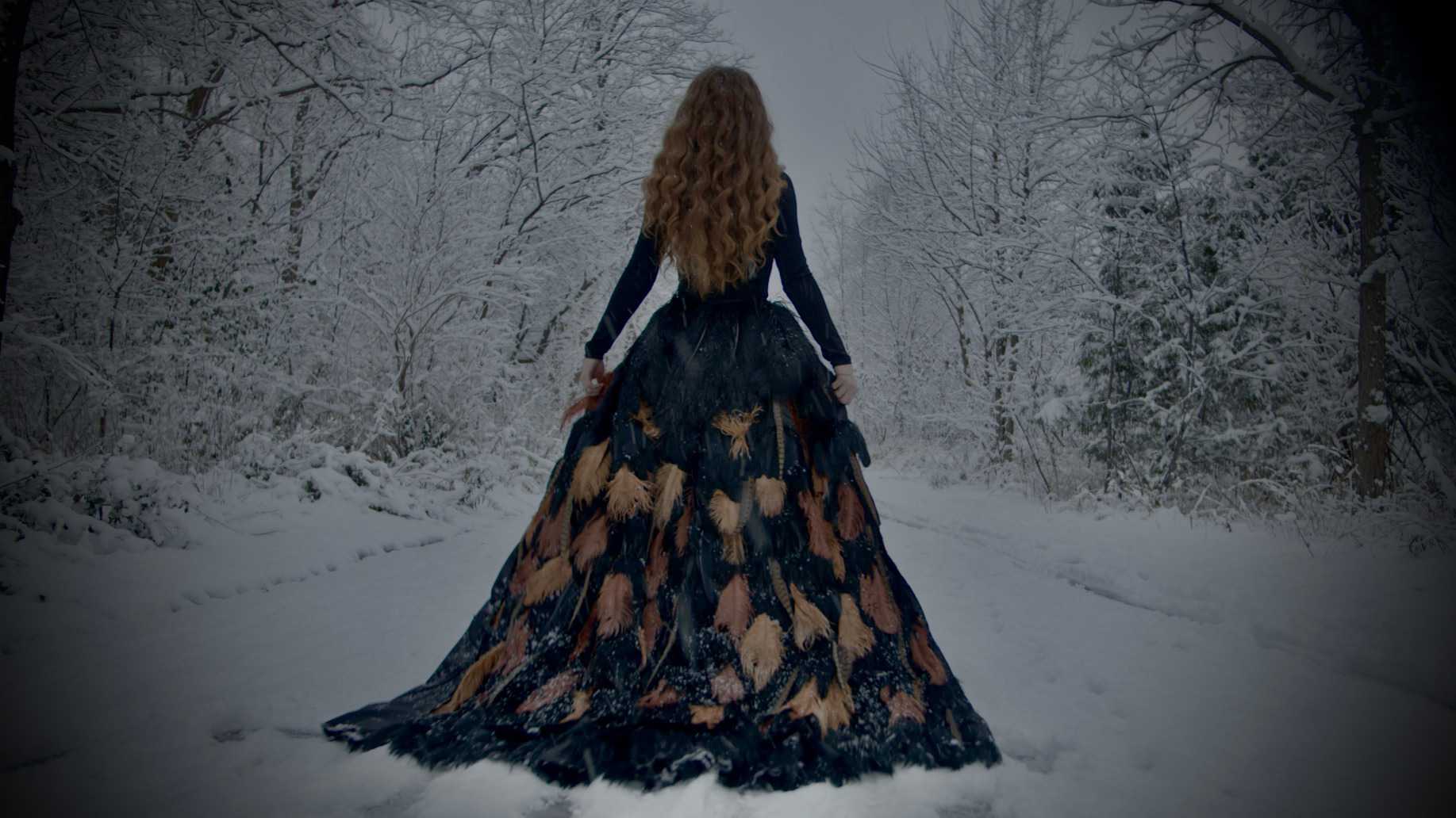 Alaina in a flowing dress standing in the forest in the snow.